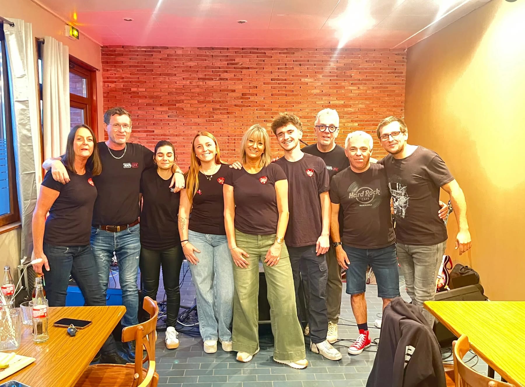 Les musiciens et l'équipe en t-shirts 100 % Live, devant le mur de briques de la salle de concert